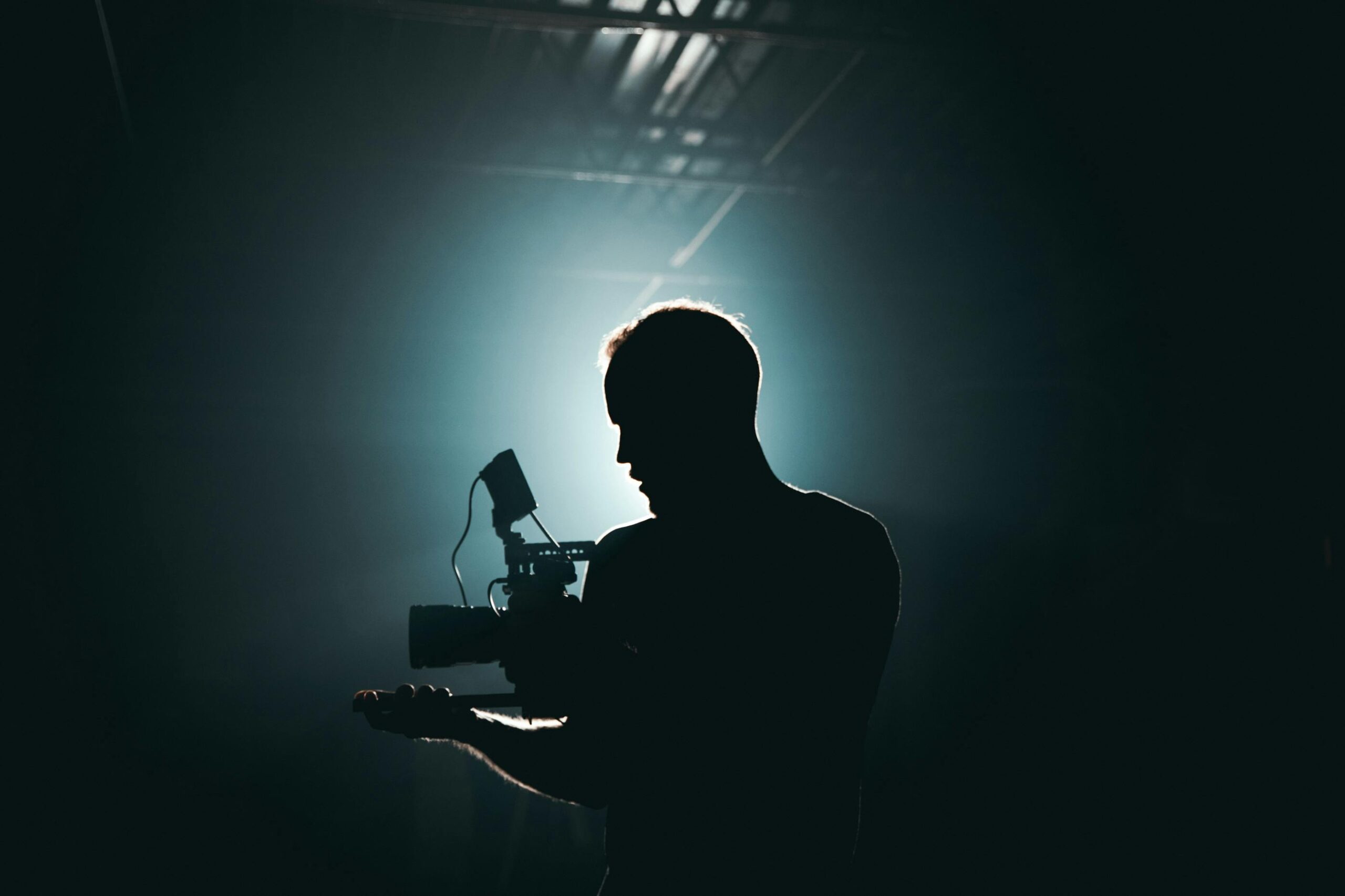 “Dramatic backlit silhouette of cinematographer with professional camera equipment”